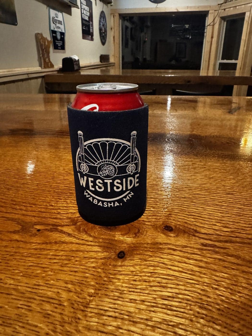A navy West Side koozie on the bar top, with the back wall and its beer signs behind it